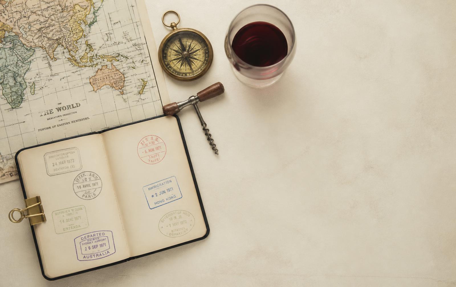 Carnet de voyage tamponné, carte du monde, boussole et verre de vin rouge